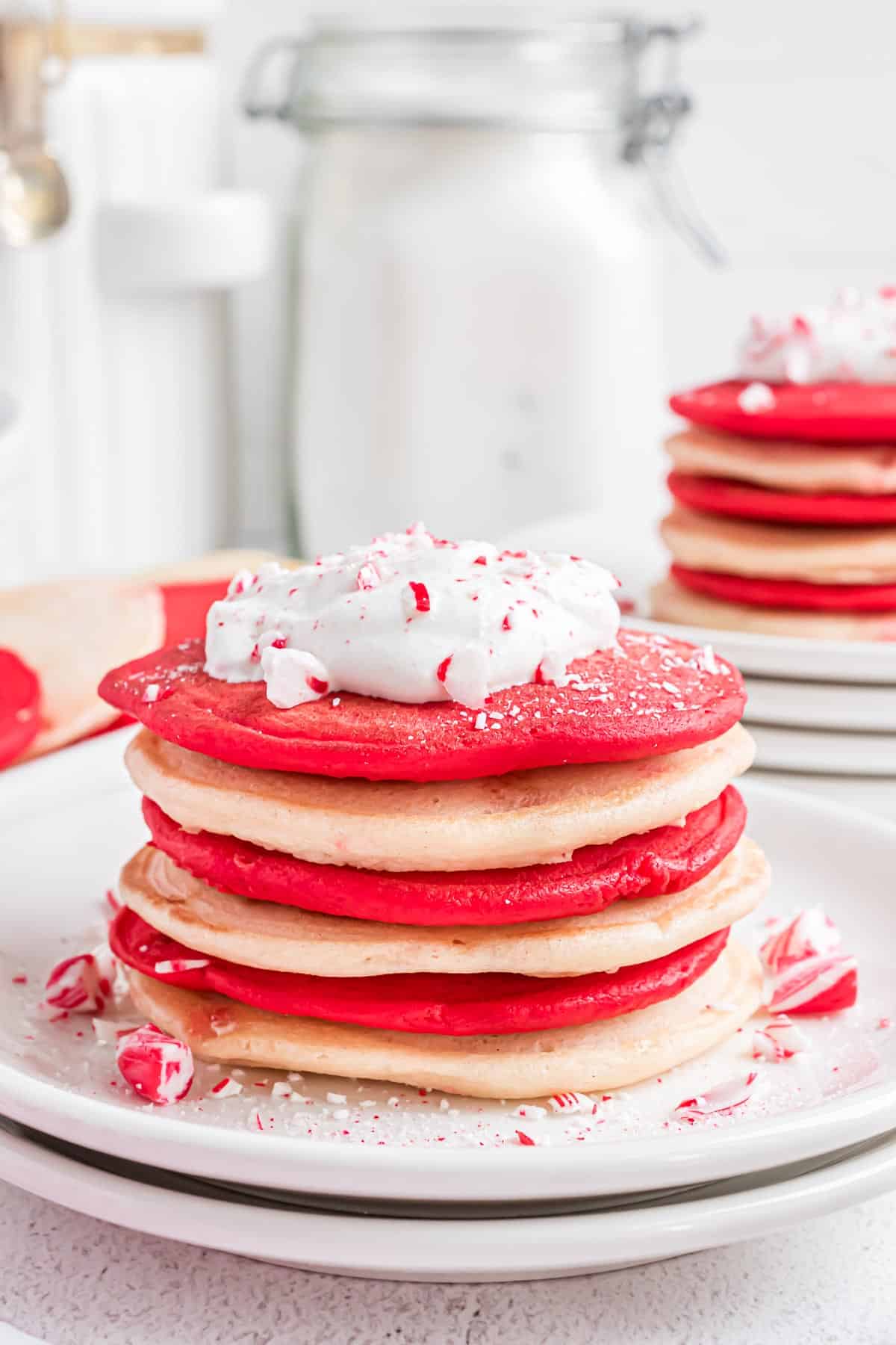 Montón de panqueques rojos y blancos cubiertos con crema batida y bastón de caramelo triturado.
