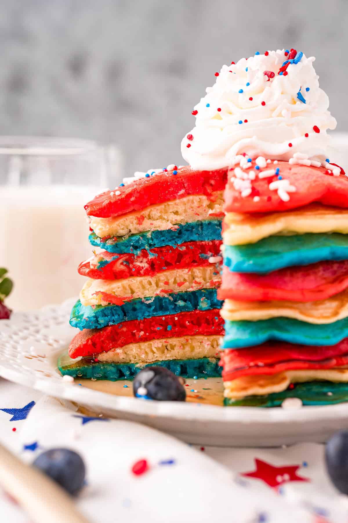 Pilha de panqueques rojos, blancos y azules decorados con crema batida y chispas.