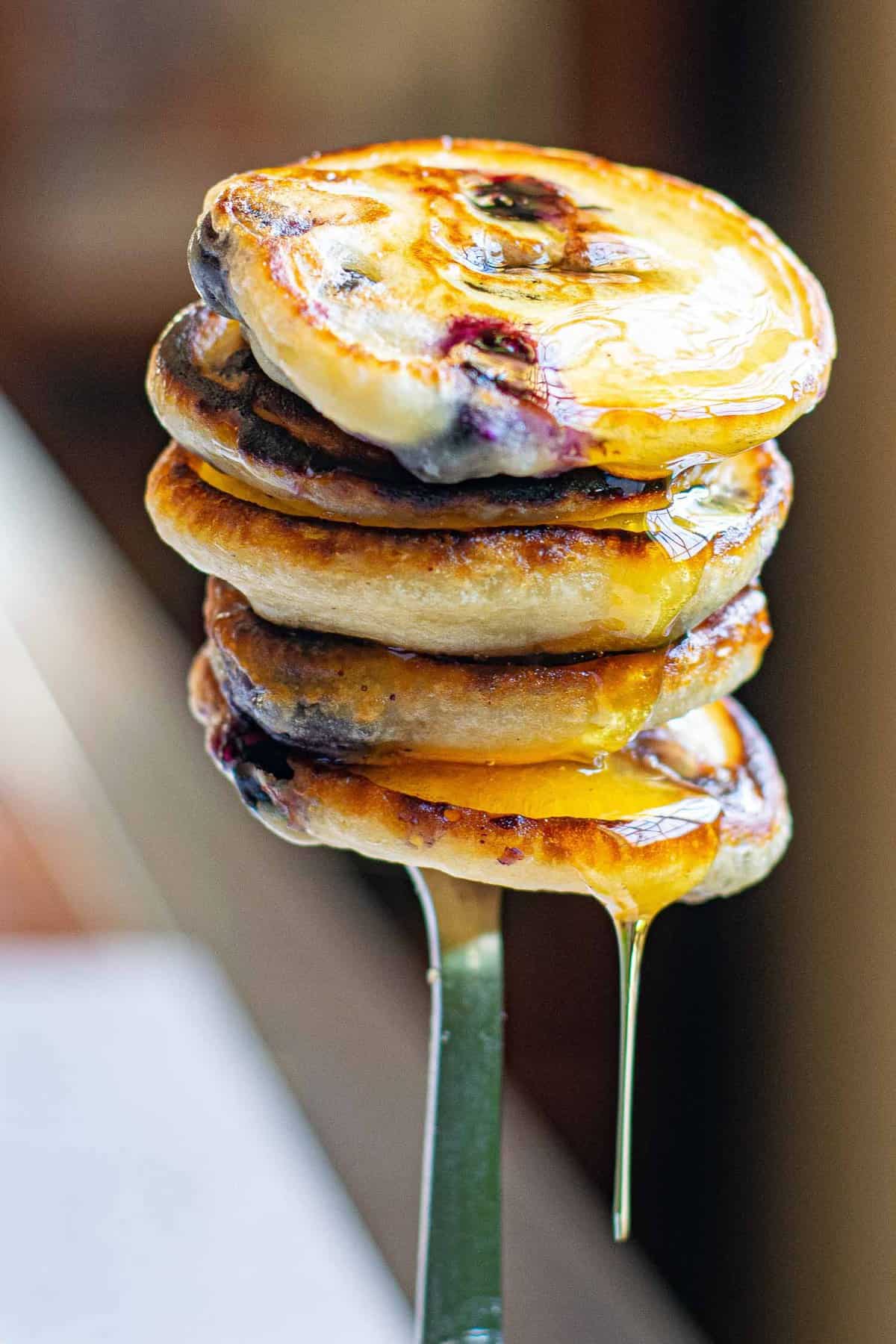 Montón de pequeños panqueques veganos de arándano en un tenedor, goteando con jarabe.