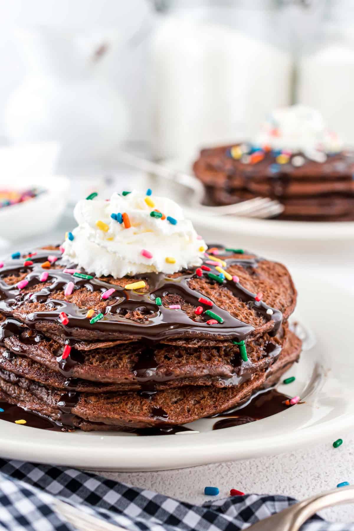 Montón de panqueques de chocolate cubiertos con crema batida, glaseado de chocolate y chispas.