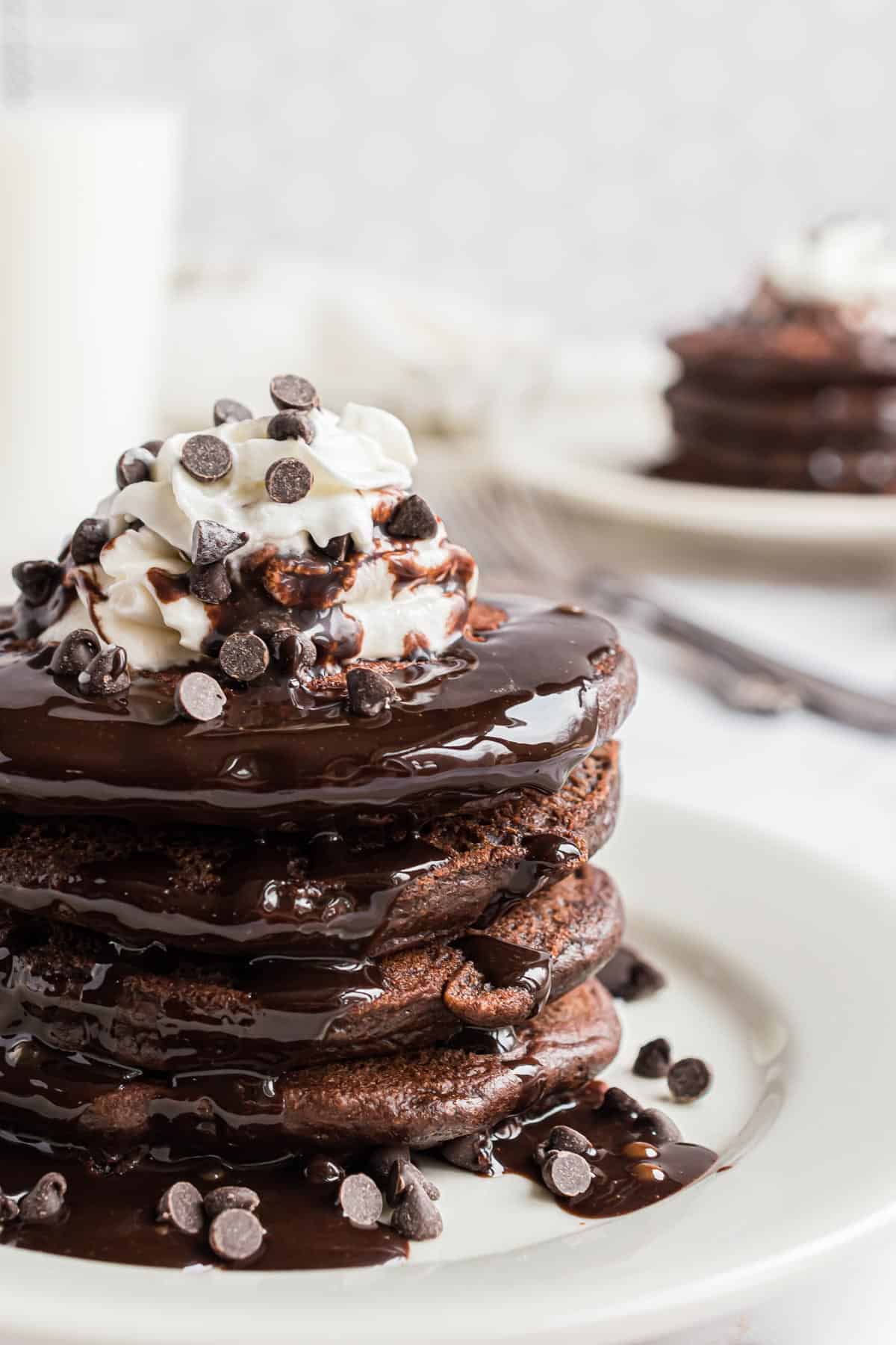 Pila de panqueques de chocolate cubiertos con crema batida, chispas de chocolate y jarabe de chocolate.