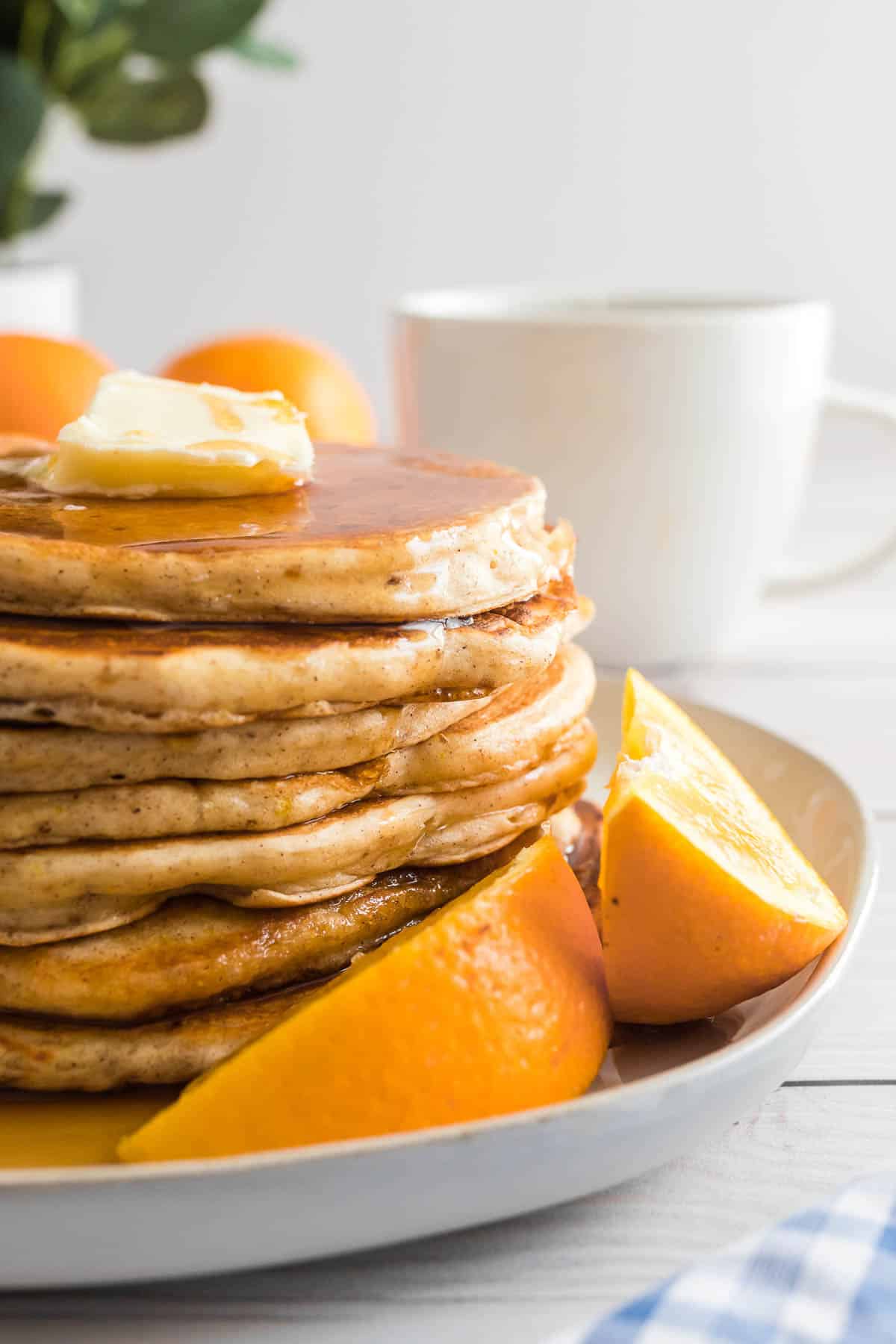 Montón de panqueques de naranja en un plato con gajos de naranja.
