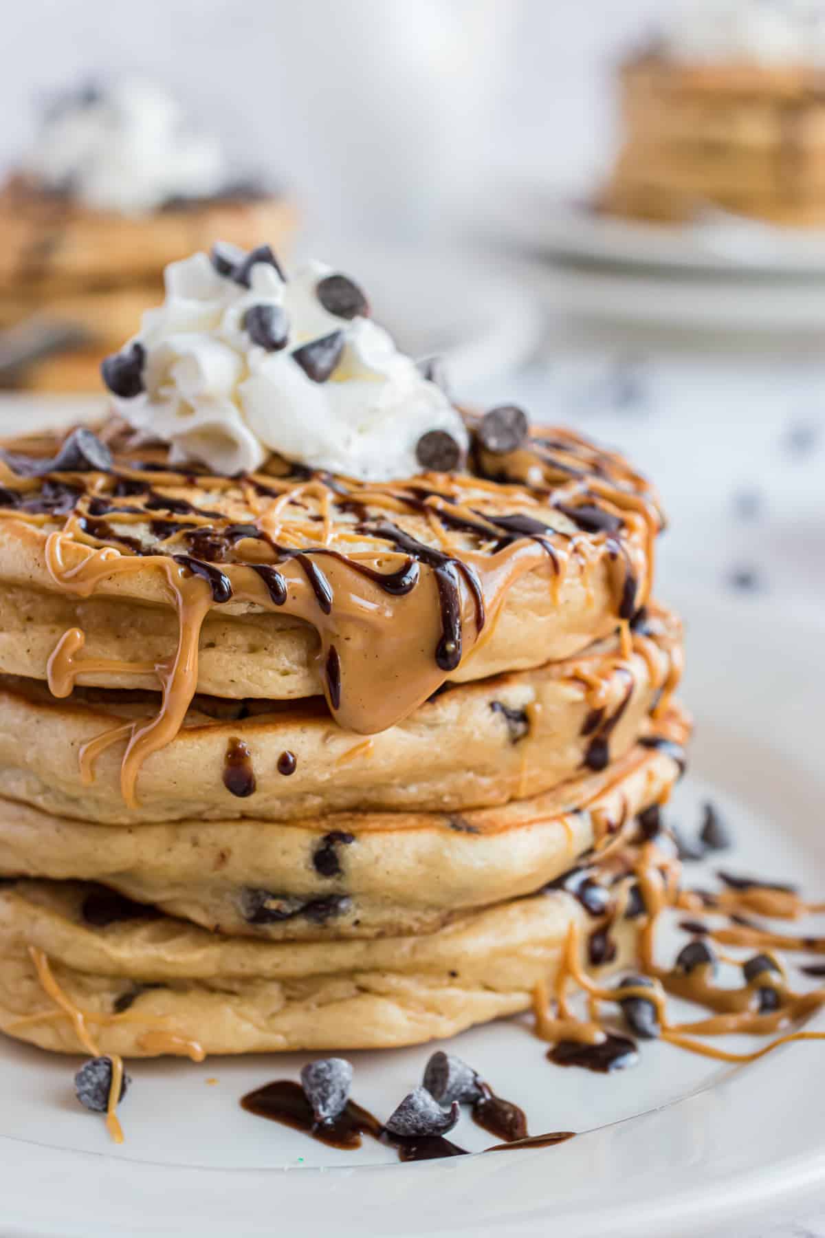 Pila de panqueques bañados en mantequilla de cacahuete y chocolate, decorados con crema batida.