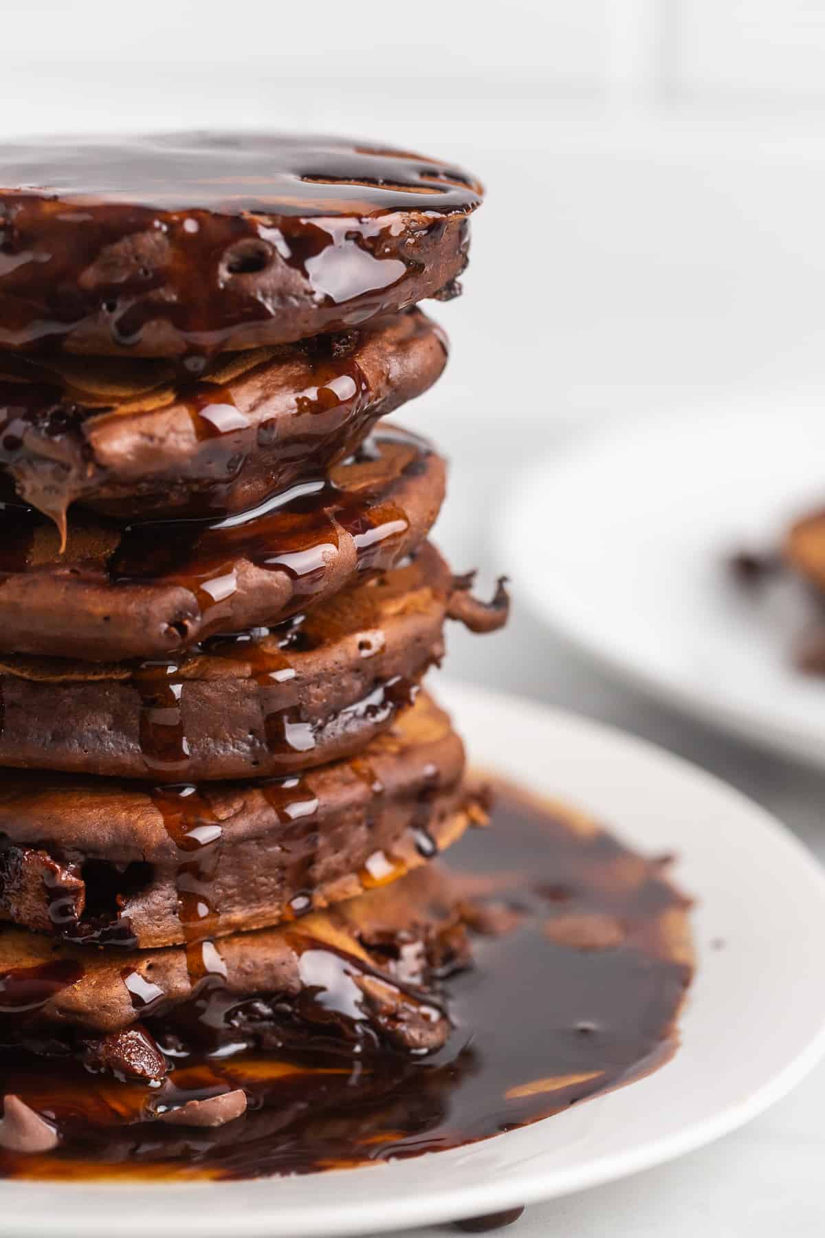 Primer plano de una alta pila de panqueques de chocolate con jarabe de chocolate.