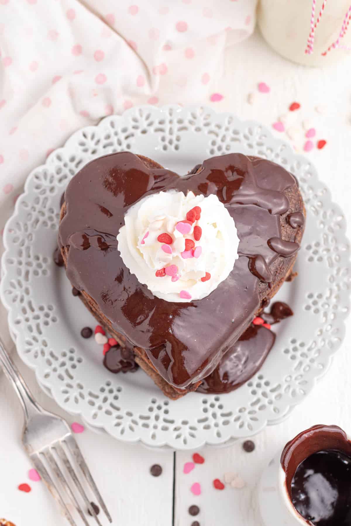 Montón de panqueques en forma de corazón cubiertos con ganache, crema batida y chispas.