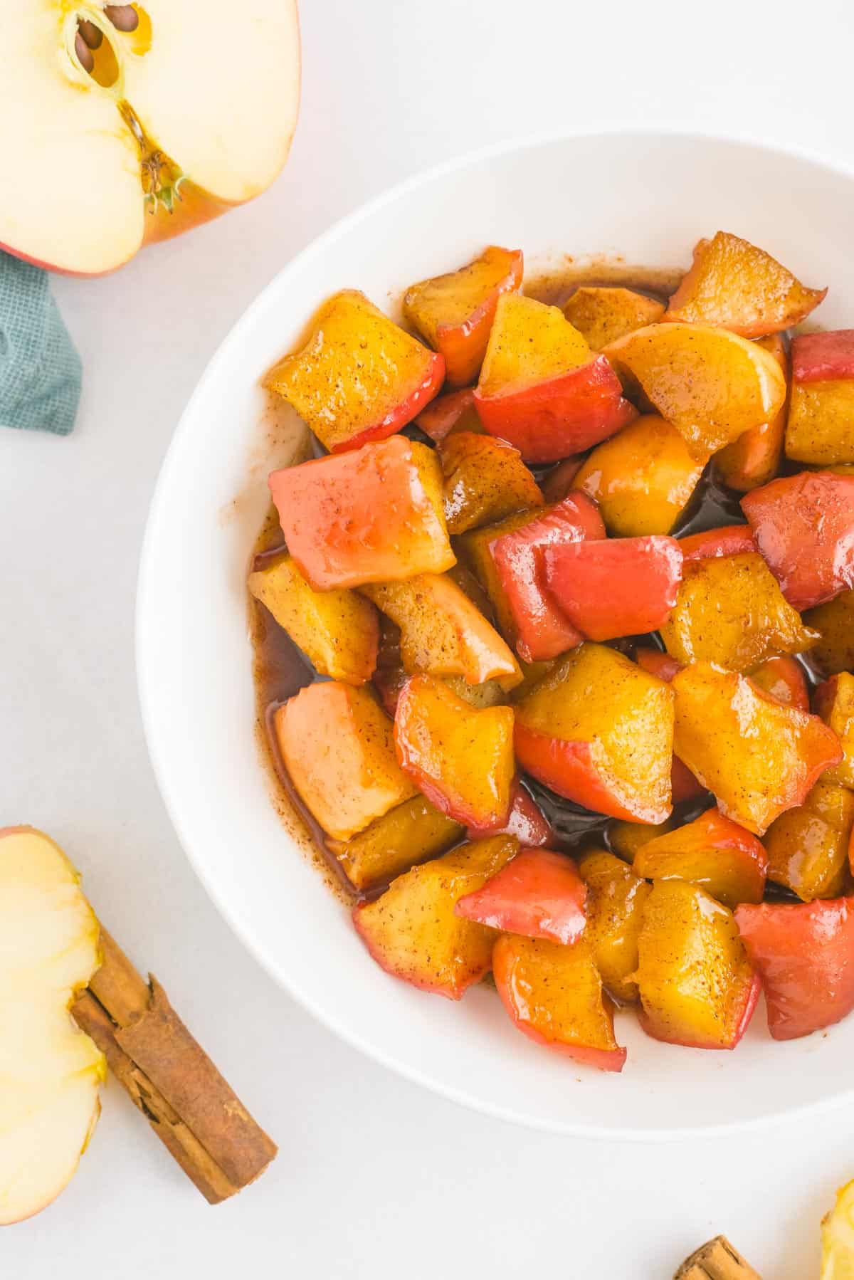 Compota de manzana con canela en un bol blanco, con mitades de manzana y palitos de canela también en la foto.