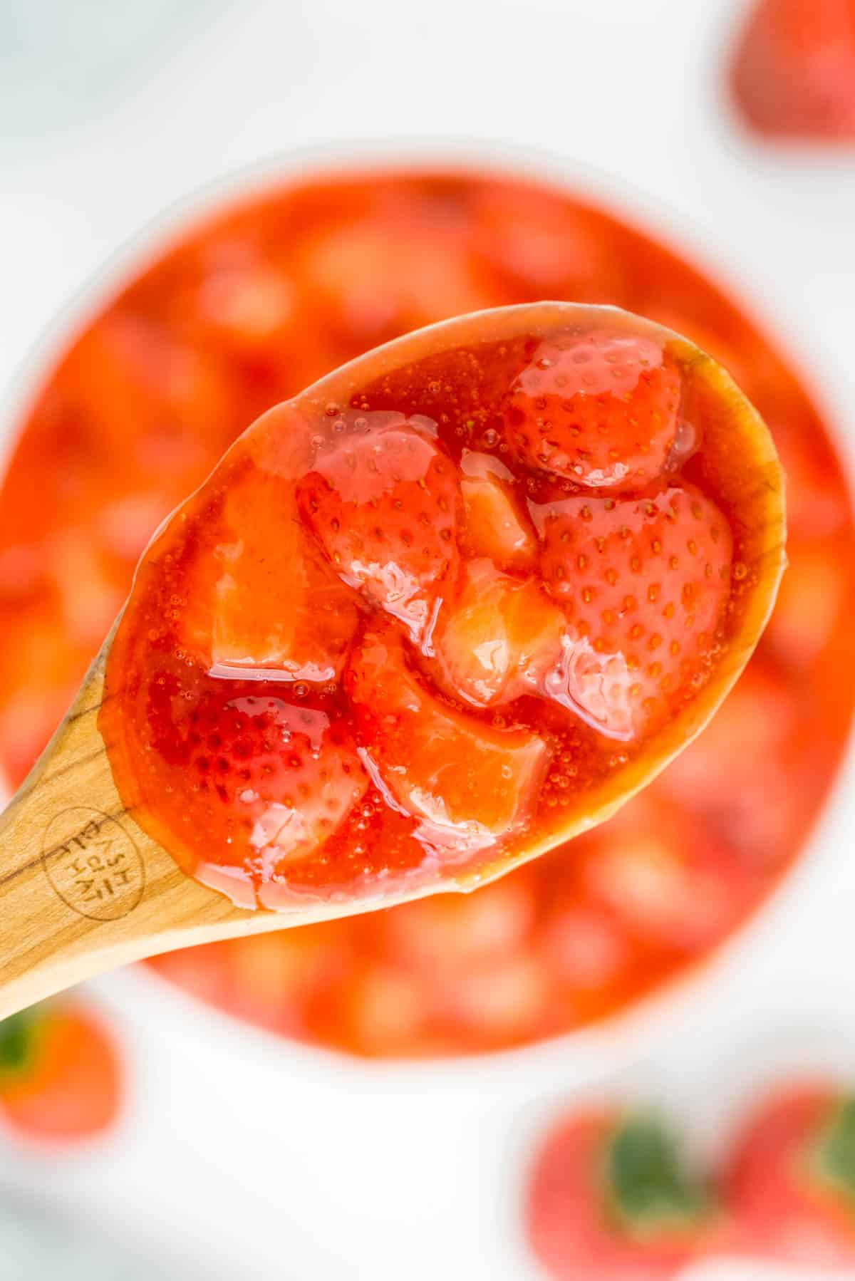 Una cuchara de salsa de fresas sostenida sobre un tazón con más.