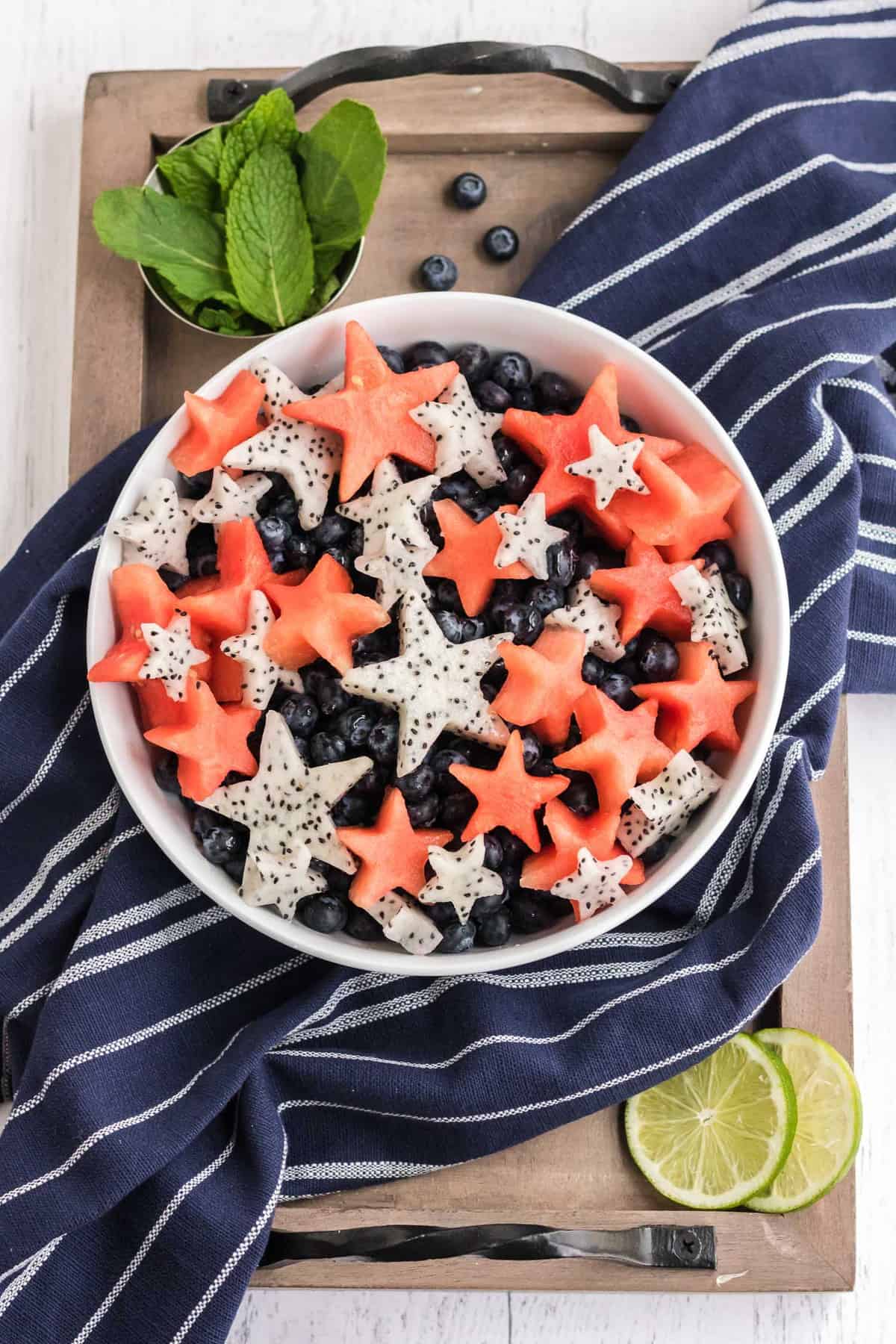 Ensalada de frutas roja, blanca y azul en un tazón blanco sobre un mantel azul.