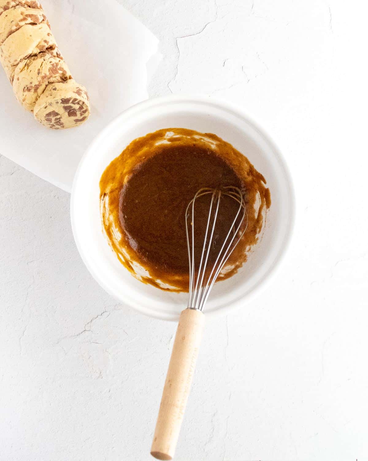 Puré de calabaza mezclado con mantequilla, azúcar moreno y especias en un tazón blanco con batidor.