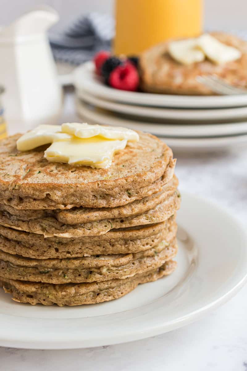 Alta pila de panqueques cubiertos con mantequilla y jarabe.