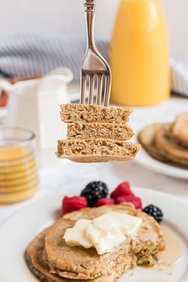 Panqueques de calabacín cortados en un tenedor, más panqueques al fondo.