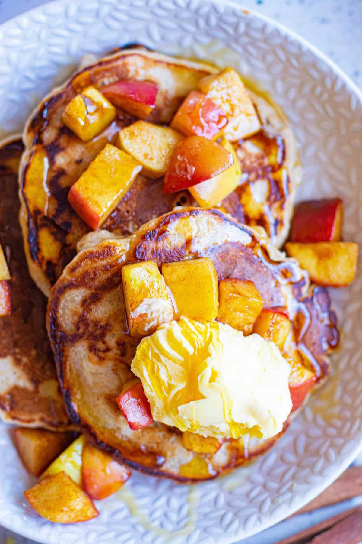 Dos pancakes en un plato cubiertos con mantequilla y manzanas salteadas.