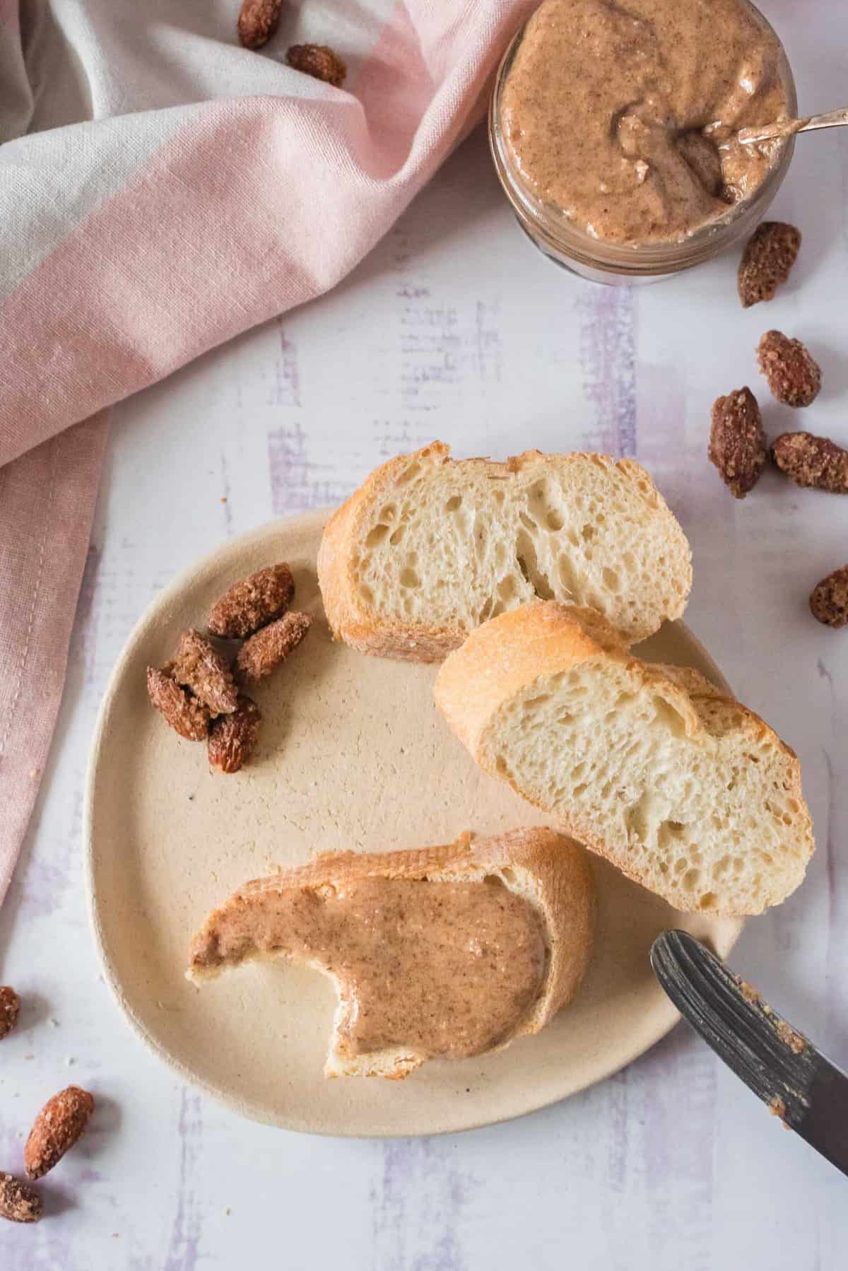 Mantequilla de almendra untada en pan con más pan y un tarro de mantequilla de almendra cerca.