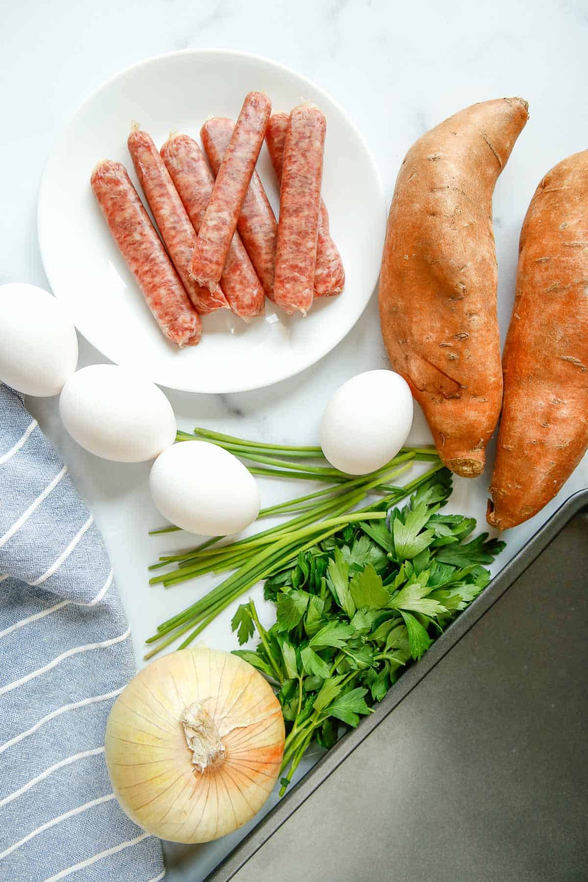 Vista aérea de batatas, salchicha, una cebolla, huevos y hierbas frescas.