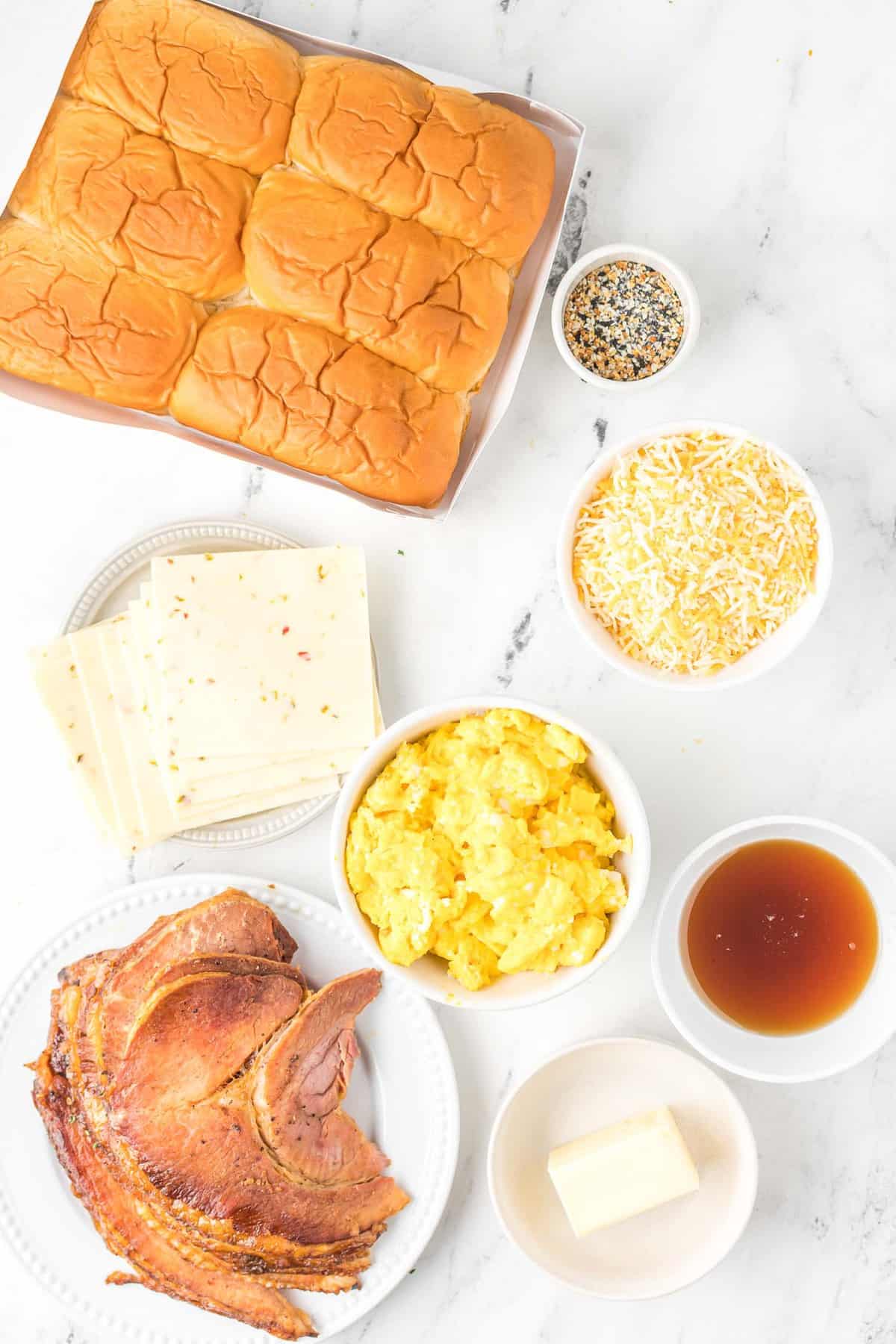 Vista aérea de los ingredientes: rollos, jamón, huevos, queso, jarabe de arce, mantequilla y aderezo para bagels todo en uno.