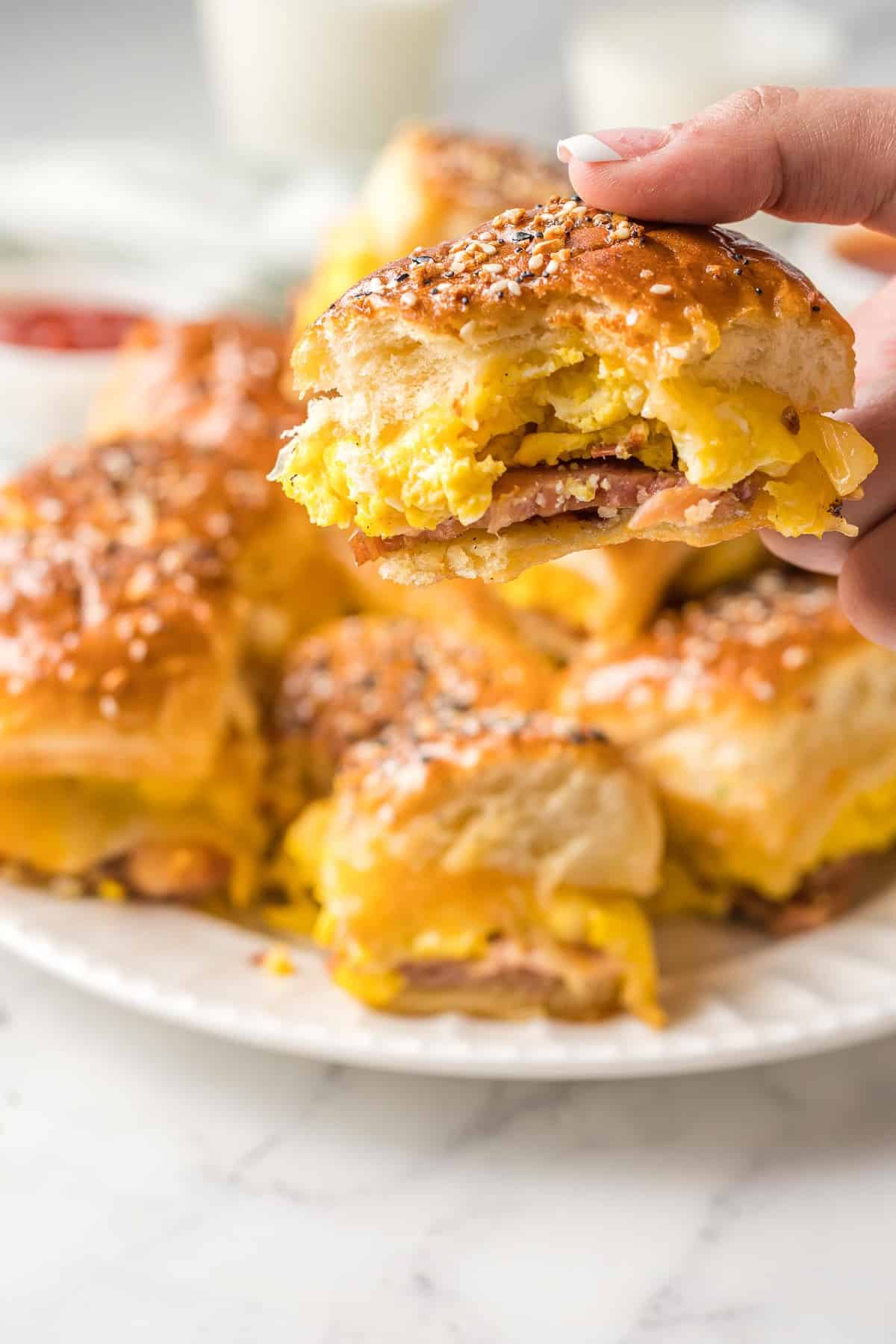 Una mano sosteniendo un slider de desayuno con jamón, queso y huevos.