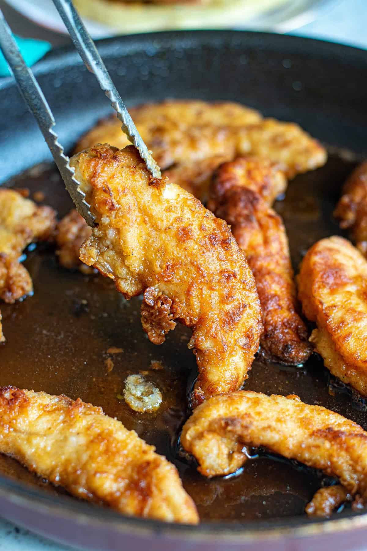 Pollo frito siendo sacado de una sartén con pinzas.