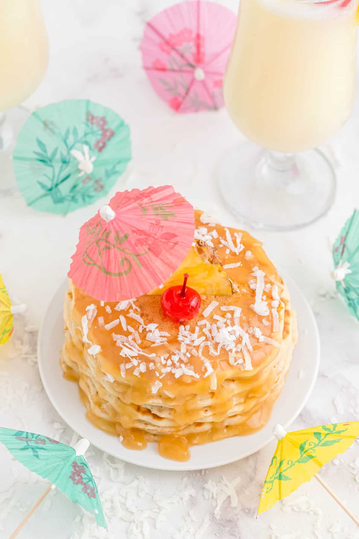 Panqueques de piña colada desde arriba, cubiertos con coco, una cereza y un paraguas de papel.