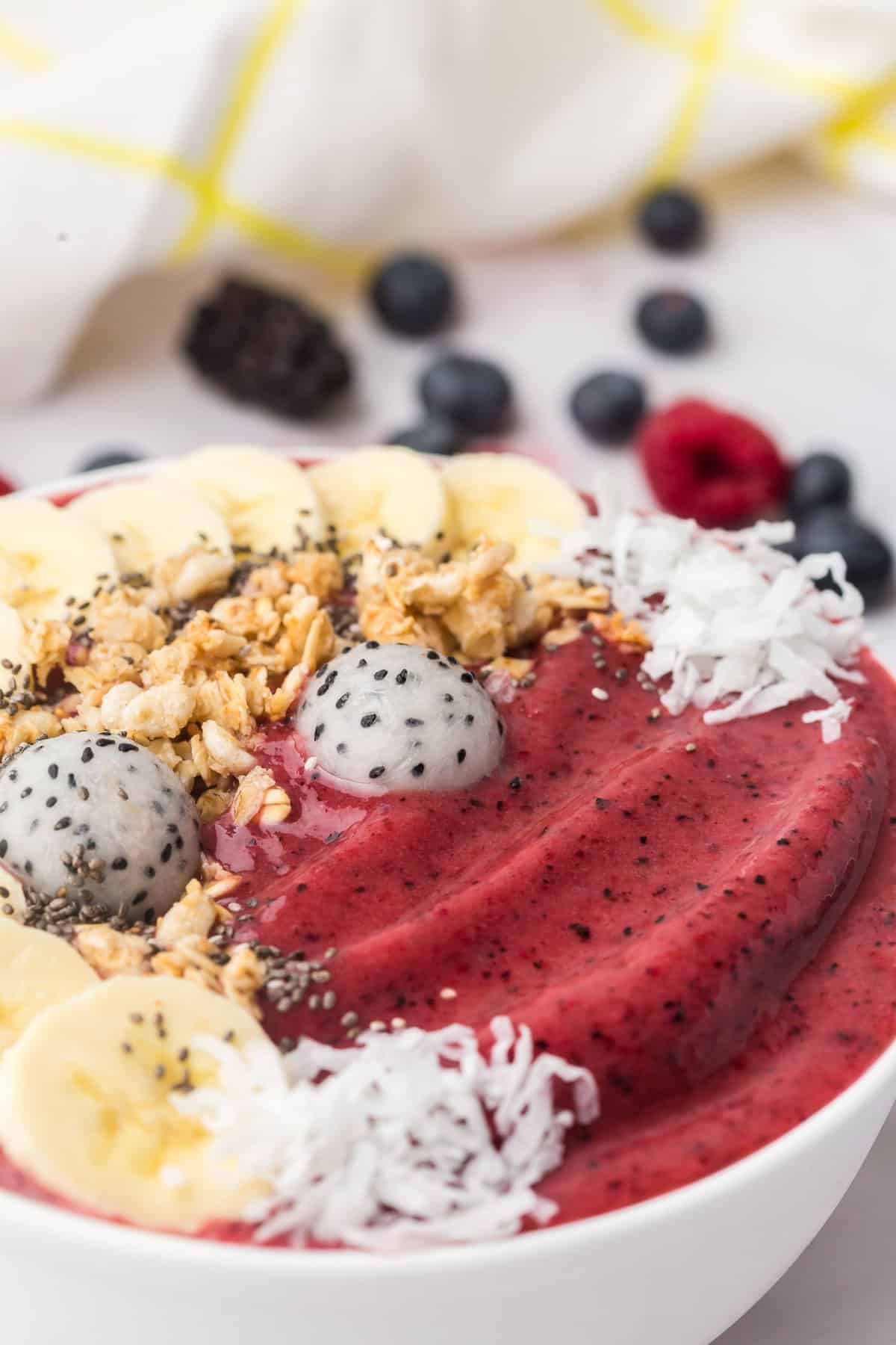 Tazón de batido rojo oscuro decorado con fruta del dragón, coco, plátanos, semillas de chía.