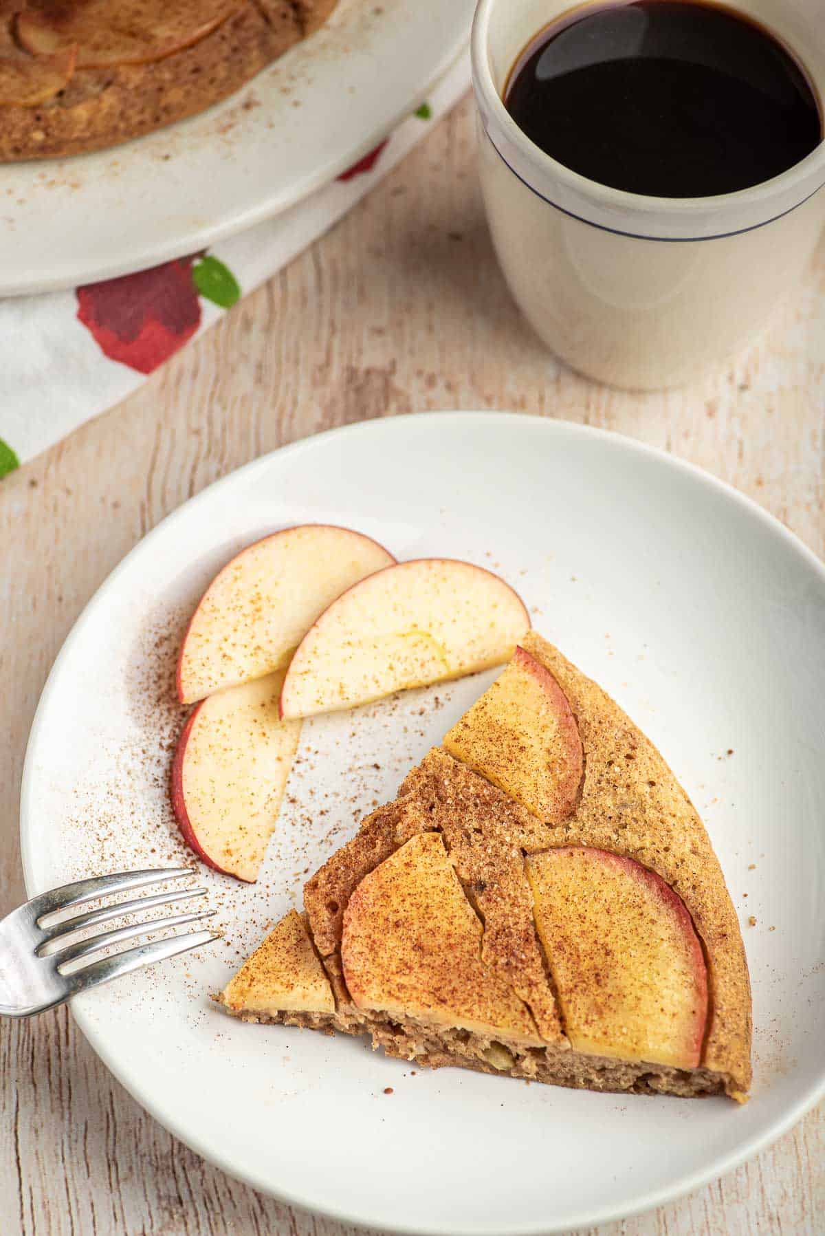 Porción de panqueque de manzana en un plato blanco con rebanadas de manzana. Café de fondo.