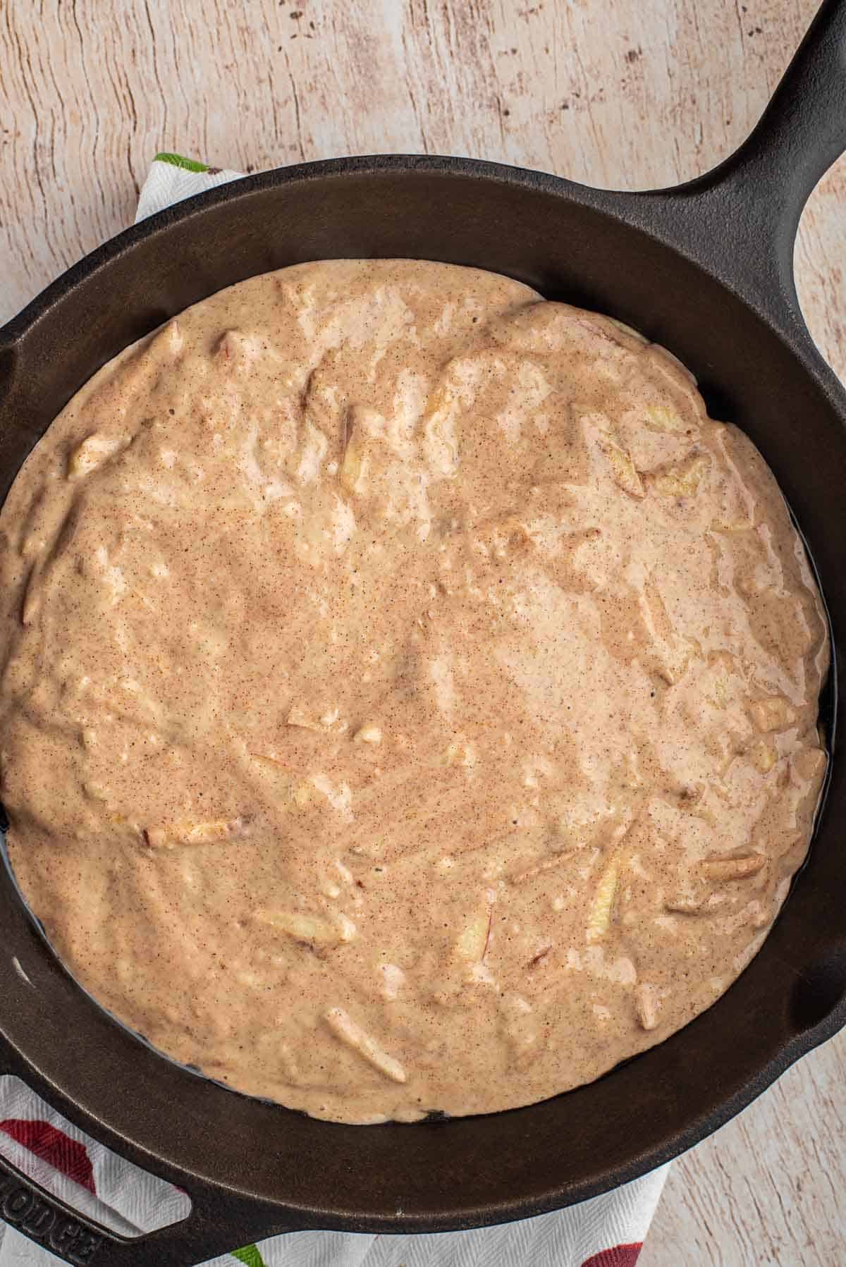 Masa de panqueque de manzana y canela en una gran sartén de hierro fundido negra.