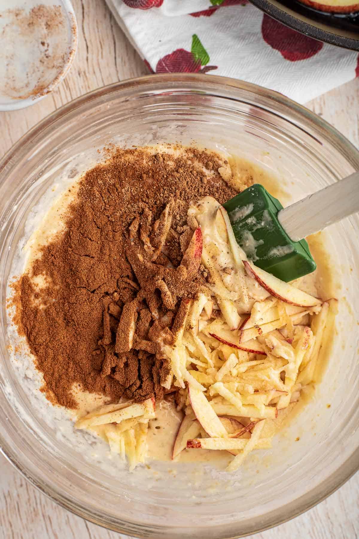 Manzanas, canela y otros ingredientes para panqueque en un gran tazón de mezcla de vidrio.