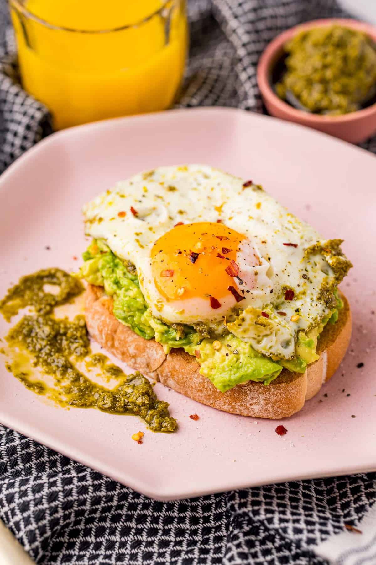 Huevo cocido con pesto sobre tostada de aguacate en un plato rosa.