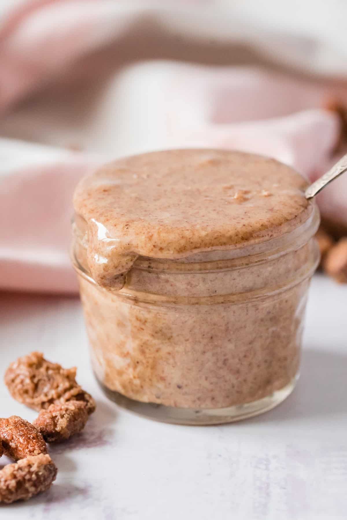 Mantequilla de almendra desbordándose de un pequeño tarro de vidrio.