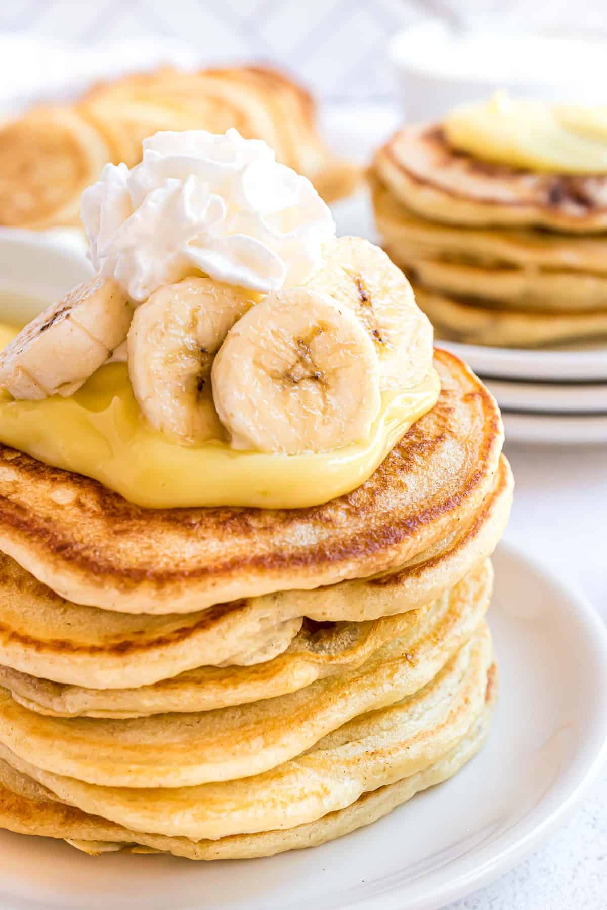 Acercamiento de la pila de panqueques cubiertos con pudín, crema batida y bananas.